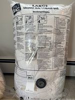 Large vacuum-seal storage bag with printed instructions and black valve containing a white duvet stored inside
