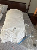 Rolled white duvet on a bed with a plastic bag beside it, showing the main duvet item.