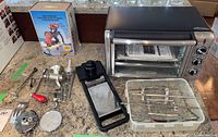 Photo shows Porkert meat mincer disassembled with parts, Black & Decker toaster oven with rotisserie prongs inside, and mandolin slicer with container on a countertop.