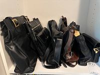 Six handbags and purses arranged side by side in a shelf, mostly black leather with one brown checkered bag visible.
