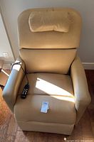 Front view of beige electric power lift recliner chair with remote on seat and lot tag.