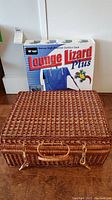 Wicker picnic basket with handle and zippers, placed on wooden surface in front of Lounge Lizard Plus outdoor seat box.