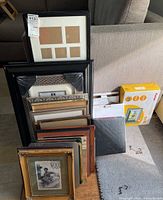 Assorted picture frames of various sizes and styles arranged against a couch, including large black rectangular frame and photo albums.