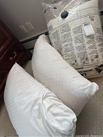 Two white bed pillows on carpeted floor near wooden furniture.