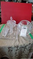 Overview of all 6 pieces showing lidded pedestal bowl, two footed bowls, vase, serviette holder and rectangular tray on textured tablecloth with red background.