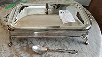 Rectangular metal serving dish with lid on table along with Oneida serving spoon in front