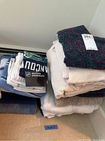 Stack of mixed bath and kitchen towels including beige, white, and blue towels with a Vancouver Canucks towel on top.