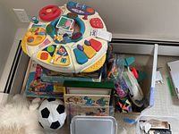 Top-down view of toys showing electronic activity center, puzzles, plush soccer ball, and various small toys arranged in a pile.