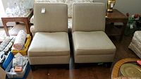 Photo of two beige upholstered chairs with wooden legs placed side by side, showing top view, seat, and back cushions.
