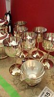 Group of six silverplate stemmed goblets with rounded bowls and wide bases shown in front of the teapot set.