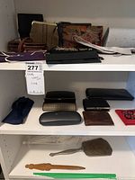 First photo shows shelves with men's and women's wallets in various materials and colors, eyewear cases, letter opener, hand mirror, and parasol on bottom shelf.