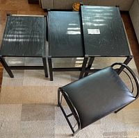 Three black wood nesting tables with rectangular tops arranged from largest to smallest showing wood grain texture and a black vinyl padded metal bench seat with tubular frame