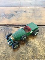 Green antique Lesney Bentley toy car with brass-colored grille, red seats, and black wheels on wood surface.