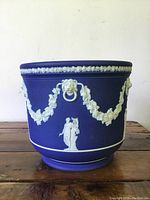 Front view of royal blue Wedgwood jasperware jardinière showing white garland and classical figure relief decorations.