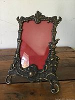 Front view of the antique Art Nouveau brass picture frame showing intricate floral and organic design elements and a red backing.