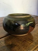 Side angle view of vintage ceramic pottery bowl showing glossy variegated dark green and brown glaze surface, rounded shape, and wide mouth opening.