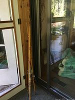 Photo showing the full length of the vintage bamboo fishing rod leaning against a wooden door and glass door, highlighting the bamboo finish and condition.
