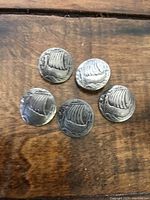 Top view showing front design of five vintage metal buttons featuring a raised sailboat motif.