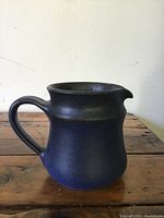 Side view of the royal blue pottery creamer showing the handle and spout on a wooden surface.