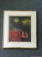 Framed print showing abstract hand-like figure in red and black with gold moon in the upper left, all set against dark smoky background.
