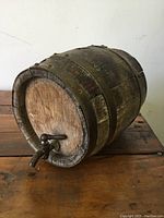 Miniature antique wooden barrel on a wooden surface, showing spigot at one end and metal bands.