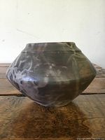 Side view of small pottery bowl showing round shape and earthy smoke-fired finish with subtle wear.