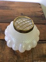 Photo of opalescent glass flower frog showing metal lattice top and textured glass body on wooden surface.