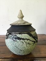 Front view of lidded Raku pottery bowl showing textured green and black glaze with light crackling on lid.