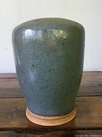 Side view of the green glazed pottery vase showing its shape, glaze patterns, and natural clay base.