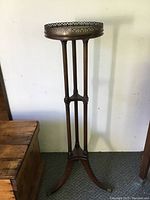 Full view of the antique Duncan Phyfe style wooden plant stand showing the three slender legs, round top with pierced gallery edge, and curved base legs with brass caps.