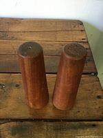 Pair of teak wooden salt and pepper shakers standing upright on a wooden surface showing wear and color variations.