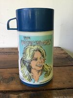 Front view of the vintage plastic thermos showing The Bionic Woman portrait and title graphic on white background with blue lid and base.