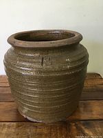 Front view of the dark green ceramic pot showing textured ridges, character mark on side, and overall cylindrical shape with wide rim.