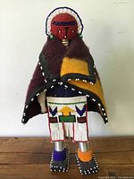 Front view of vintage handmade Kachina doll with red beaded head and wool blanket