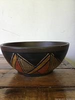Side view of the ceramic bowl showing brown base color with hand painted orange and beige geometric pattern.