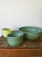 Five vintage plastic salad bowls on wooden surface; one large muted green round bowl and four smaller bowls in muted green and light yellow-green.