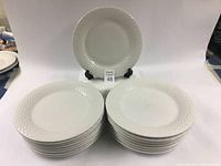 Stack of 17 white porcelain dinner plates with one plate displayed on an easel showing textured rim design.