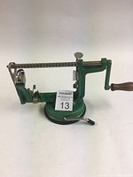 Side view of the vintage green metal apple peeler showing the crank, wooden handle, peeling rod and suction cup base.