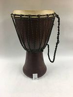 Front view of the Djembe drum showing carved wooden body and black braided rope tuning system.
