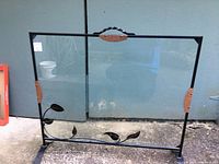 Photo showing the full handcrafted fireplace screen with black metal frame, glass panel, and decorative brown leaves at corners and bottom left.