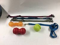 Full view of three dog collars laid horizontally with three dog chew toys in front of them on a white surface.