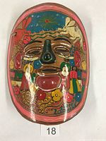 Front view of the oval pottery mask showing colorful painting with animals and decorative motifs.