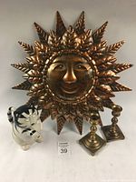 Group photo of sun wall art, cat figurine, and brass candlesticks