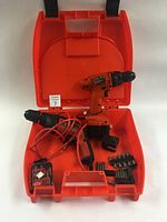 Photo showing cordless drill, battery pack, charger, drill bits, screwdriver bits, and open orange plastic carry case holding all items.