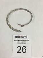 Braided sterling silver bracelet laid flat in a circular shape with auction lot number card beneath.
