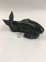 Side view of the black whale carving showing the whale's fluke and one pectoral fin with visible chips and repaired cracks.