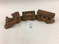 Three connected pieces of a vintage handmade wooden toy train: an engine, flatbed car, and passenger car on a white background with lot number card.