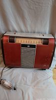 Full view of the 1953 RCA Victor radio showing its red body, speaker grille, tuning dial, and attached power cord.