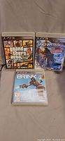 Three PS3 game cases showing Grand Theft Auto V, Uncharted 3, and Brink titles