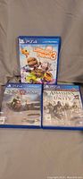 Three PS4 game cases with cover art. LittleBigPlanet 3 on top center, God of War bottom left, Assassin's Creed Unity bottom right.